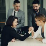 Two women arm wrestling with men watching them