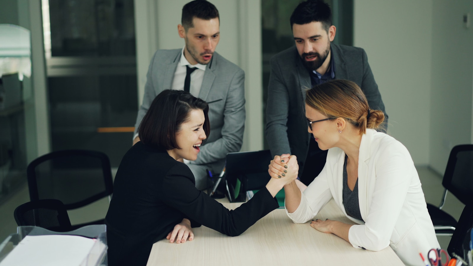 Two women arm wrestling with men watching them